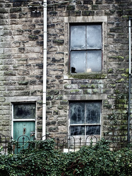 derelict abandoned house with broken windows and ivy growing up the walls with a green wooden door and stone walls in england