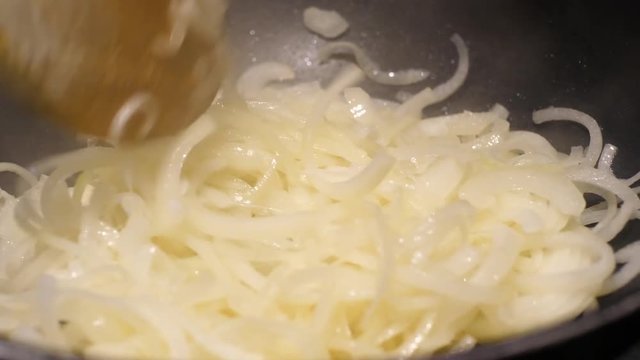 close up of onions in a frying pan being stired with wodden spoon