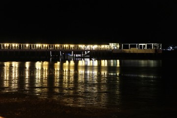 Fototapeta na wymiar The night light at the bridge reflection on the beach 