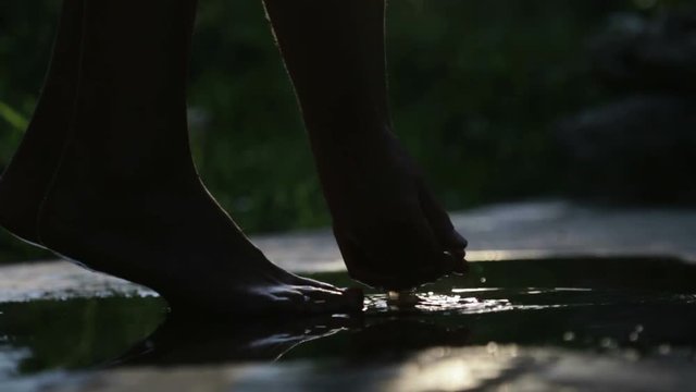 Silhouette of a woman playing in a puddle of water. Close up of female hands and feet near a puddle with water in backlight.
