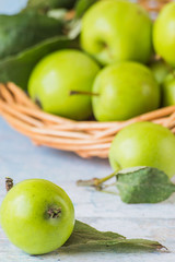  Fresh green apples with leaves in a wicker basket on a light wooden table. A new crop.