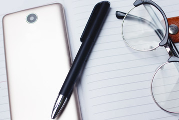 Smartphone , Ballpen And Black Eyeglasses Over Management Diary