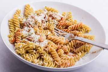 A half full white plate, with fusilli, covered with tomato sauce and parmesan