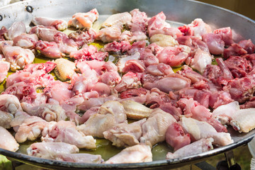 Process of frying rabbit and chicken juicy meat slices in olive oil in large flat paella skillet. Burner with open fire. Weekend picnic setting, summer. Lifestyle.