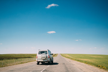 Fototapeta na wymiar Gray SUV Car rides along Road In Spring Summer Fields Landscape
