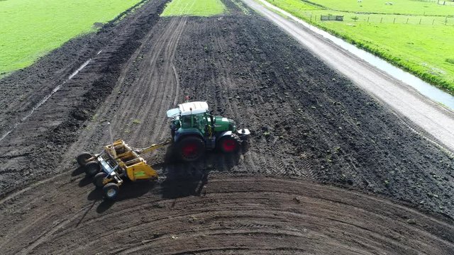 Aerial bird view of tractor plowing the dark soil driving from left to right also showing seagulls flying through footage farmer is flattening land for planting crops and further food production 4k