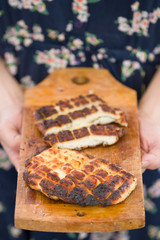 Top view on two grilled slices of homemade halloumi cheese on wooden borad in woman's hands. Outdoors. Grilling season. Healthy eating.