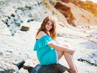 girl in a turquoise dress sitting on a rock by the sea