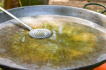 Large flat frying pan or skillet for paella or jambalaya on gas burner. Process of heating olive oil for cooking meat and vegetables with rice. Summer picnic in nature, lifestyle.