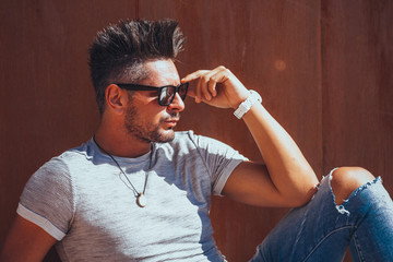 Portrait of handsome young man in casual clothing with sunglasses sitting on wood bench, looking away to a side. Color Toned Image. Concept urban man.