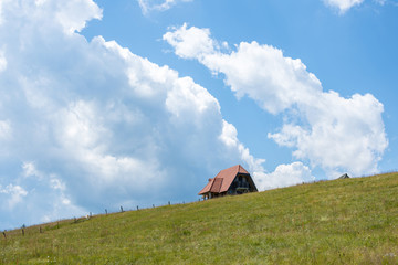 Stone Cottage on the Meadow Hill. Summer Landscape Clouds and Blue Sky.