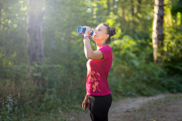 Girl drinking from a shaker during the training in the forest