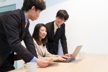 Fototapeta premium ノートパソコンの画面を見て計画を話し合う3名のビジネスパーソン