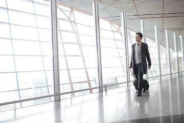 Businessman pulling wheeled luggage in airport lobby