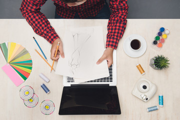 Male fashion desginer working at desk with fashion sktech. Top view.