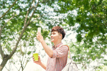 Fototapeta premium Handsome college student with backpack standing in profile and looking at camera with toothy smile, waist-up portrait
