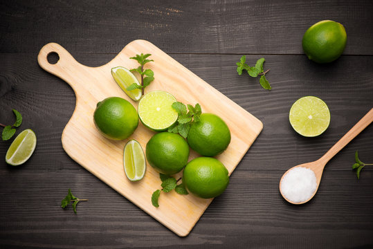 Fresh limes on cutting board on wooden table with spoon of salt. Top view, background.