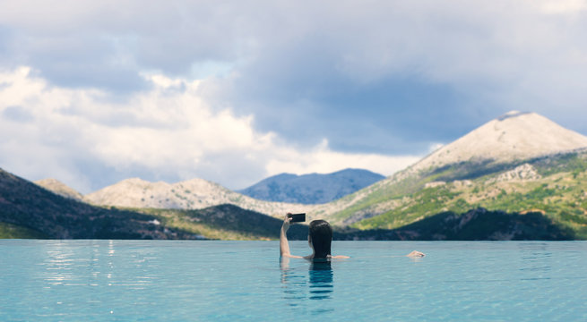 Young female in the pool on the roof on the background of Landscape of Mountains and clouds of South Tyrol