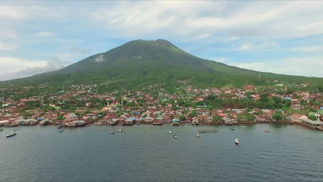 Aerial view of tropical island Ternate with Gamalama volcano in the middle, Indonesia. Shot with drone on cloudy day with blue sky, fly forward.