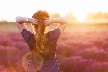 Young woman touching her long sombre hair looking at lavender field at sunset