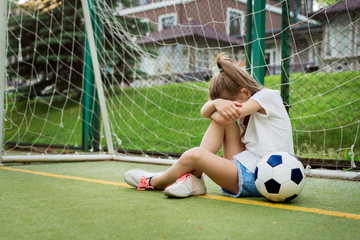 Crying ltittle girl who is playing football, hiding her face while being upset to miss goal in...