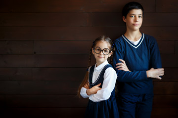 Attractive boy keeping his hands crossed while standing near his little sister in big glasses and...