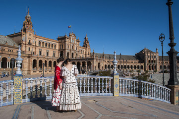 Naklejka premium Spagna: ragazze sivigliane di spalle in abiti tipici in Plaza de Espana pronte per la Fiera di Siviglia (Feria de abril) che inizia due settimane dopo la Settimana Santa di Pasqua