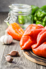Ripe peppers and garlic, glass jar on wooden board ready for preservation. Canning and preserving vegetables. Selective focus, space for text.