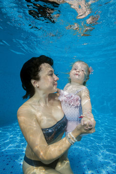 Mom with little daughter posing under water in pool
