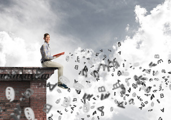 Man on roof edge reading book and symbols flying around