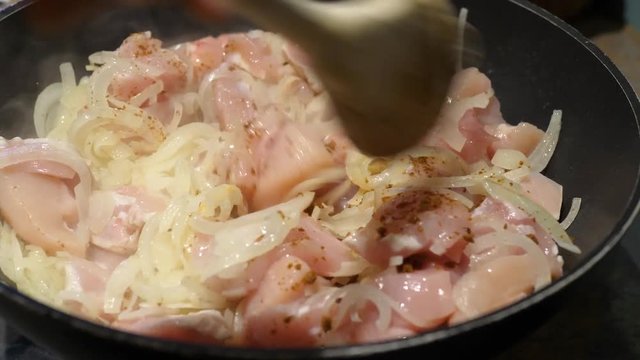 Chicken frying in a pan with onion and spices