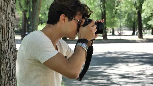 Handsome young male photographer taking photograph with professional photo camera hanging from his neck