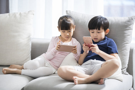 Happy boy and girl playing smart phones in sofa