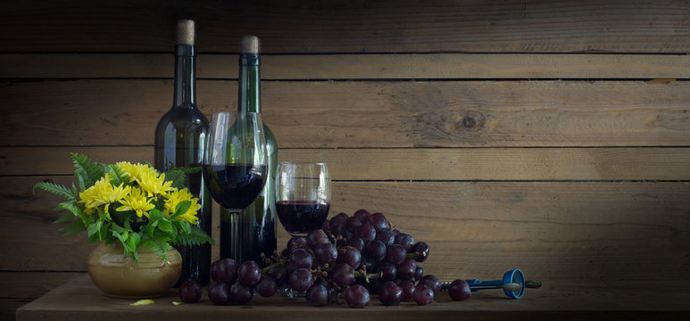 Wine Grape in the bottle and glass with fresh grape and yellow flower in vase all put on the wooden plank in dim light room