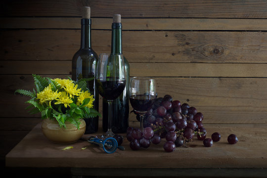 Wine Grape in the bottle and glass with fresh grape and yellow flower in vase all put on the wooden plank in dim light room