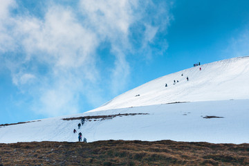 Hiking tourists climbs to the snow-capped mountain top. Concept theme: nature, weather, climbing, tourism, extreme, healthy lifestyle, adventures. Unrecognizable faces.