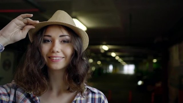 pretty young American girl stands in a shirt and hat in the Parking garage and smiles