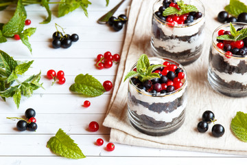 A sweet dessert of sponge cake with cream in a glass with fresh berries on wooden background