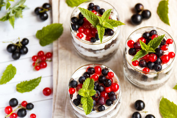 A sweet dessert of sponge cake with cream in a glass with fresh berries on wooden background