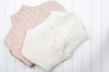 Two modern knitted sweaters on white wooden background.