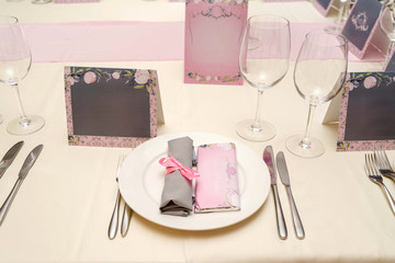 Rolled table napkin with pink ribbon and bar of chocolate with blank space for text on white plate. Table setting, free space. Table served for wedding banquet, close up. Paper blank cards for guests