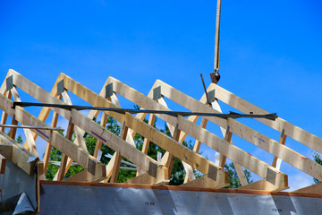 Wooden house trusses being set by a boom truck with a blue sky background. © Emily