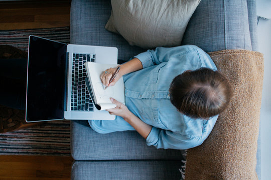 Young female entrepreneur works on business homework study fro home on couch with mobile phone