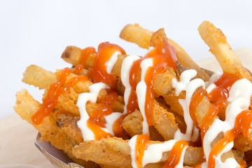 Hot and spicy french fries on a white plate with mayonnaise and tomato chili sauce