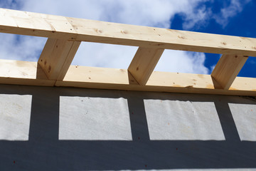 Roof gable wooden framing, against blue sky with clouds.