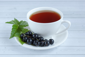 Cup of tea and black currant on a wooden background.