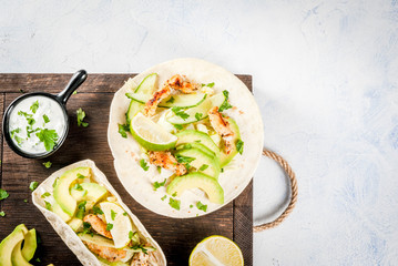 Healthy food snack. Tortillas taco with grilled chicken, avocado, fresh salsa, lettuce, lime. With yogurt & parsley sauce. On light gray stone marble table, wooden cutting board. Top view copy space