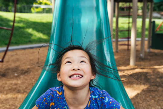 Young Asian American girl on playground slide with hair standing up from static electricity