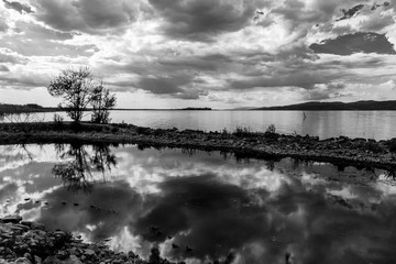 A dock in a lake, with a beautiful, deep sky with clouds reflecting on water, along with some trees