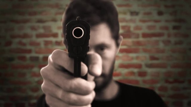 Man Pointing Gun At Camera On A Brick Wall. Man pointing a gun straight to the camera on a brick wall background